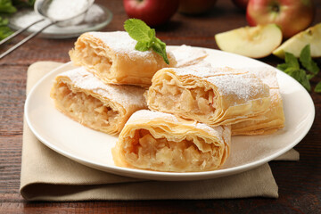 Pieces of tasty apple strudel with powdered sugar and mint on wooden table, closeup