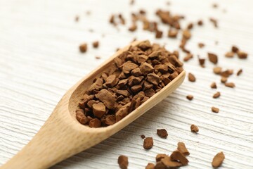 Spoon with granulated instant coffee on white wooden table, closeup