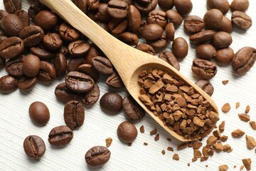 Spoon with granulated instant coffee and beans on white wooden table, above view