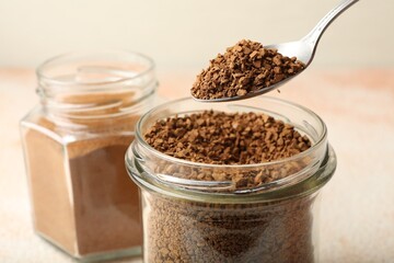Spoon with granulated instant coffee and jars on light table, closeup