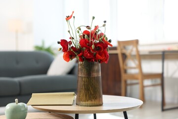 Beautiful poppy flowers in vase and book on wooden table at home