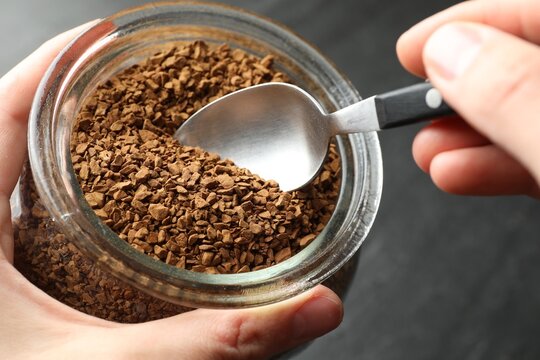 Woman taking instant coffee from jar at table, closeup - Powered by Adobe