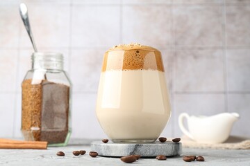 Delicious dalgona coffee in glass, beans, granules and cinnamon on grey table, low angle view