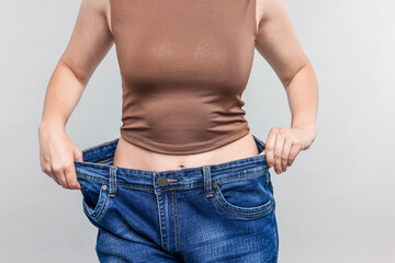 Woman wearing old jeans after weight loss on light grey background, closeup