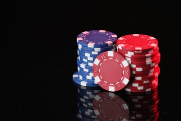 Casino chips on mirror surface against black background, closeup. Space for text