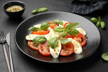 Tasty salad Caprese with mozzarella, tomatoes, basil and spices on black table, closeup