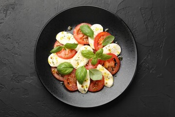 Tasty salad Caprese with mozzarella, tomatoes, basil and spices on black table, top view