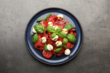 Tasty salad Caprese with mozzarella, tomatoes, basil and balsamic vinegar on grey table, top view