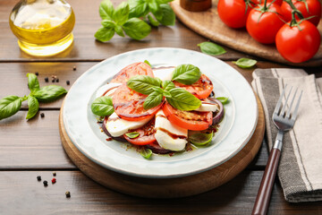 Tasty salad Caprese with mozzarella, tomatoes, basil and spices on wooden table, closeup