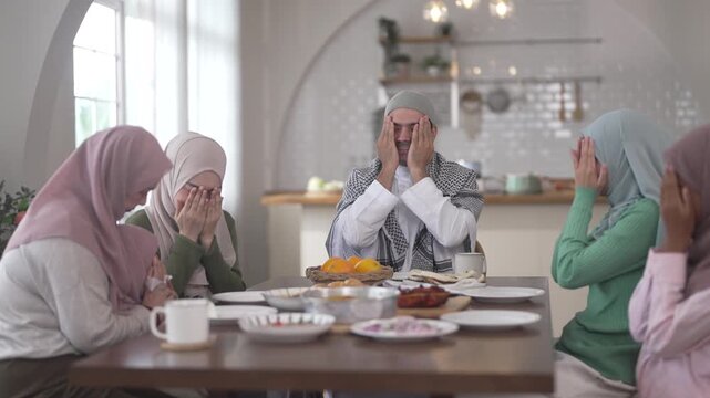 Muslim family praying before eating iftar meal during ramadan or eid together around dining table, tradition faith gratitude love, islamic culture peaceful moment with food and family, halal food