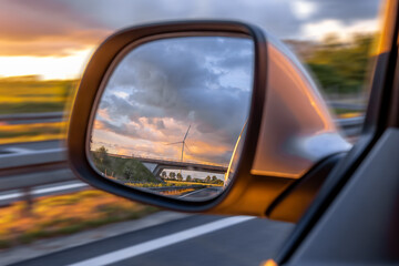 Windmill in car mirror. Sunset light. Eco energy in motion