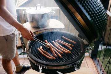 Man grilling sausages on a ceramic grill on the balcony during summertime