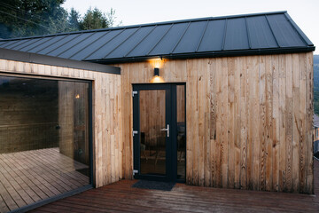 Modern wooden cabin exterior with large glass door and deck