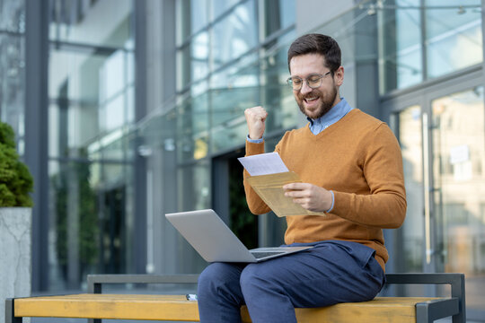 A satisfied young man sits on a bench and reads the letter he received