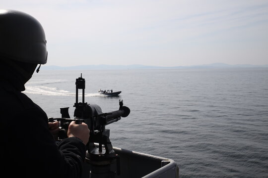 A military soldier defends a warship from an attacking boat.
