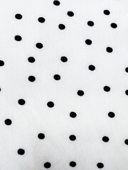 A detailed close-up of soft white satin fabric with classic black polka dots. Elegant, retro-style textile background for fashion or design use