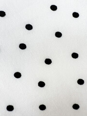 A detailed close-up of soft white satin fabric with classic black polka dots. Elegant, retro-style textile background for fashion or design use