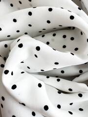 A detailed close-up of soft white satin fabric with classic black polka dots. Elegant, retro-style textile background for fashion or design use