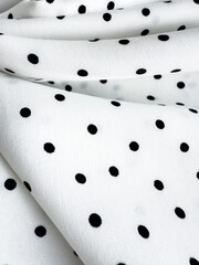 A detailed close-up of soft white satin fabric with classic black polka dots. Elegant, retro-style...