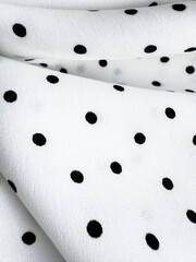 A detailed close-up of soft white satin fabric with classic black polka dots. Elegant, retro-style...
