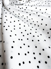 A detailed close-up of soft white satin fabric with classic black polka dots. Elegant, retro-style textile background for fashion or design use