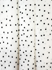 A detailed close-up of soft white satin fabric with classic black polka dots. Elegant, retro-style...