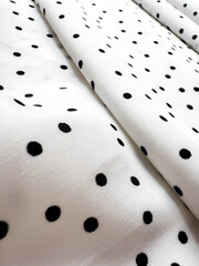 A detailed close-up of soft white satin fabric with classic black polka dots. Elegant, retro-style...