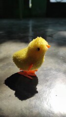 Close Up of a Small Yellow Fluffy Chick Toy with Orange Feet on a Grey Surface