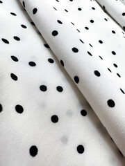 A detailed close-up of soft white satin fabric with classic black polka dots. Elegant, retro-style...