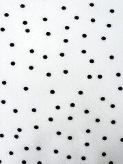 A detailed close-up of soft white satin fabric with classic black polka dots. Elegant, retro-style textile background for fashion or design use