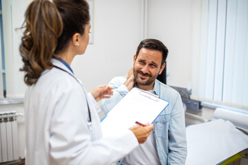 male patient points to his neck in pain while a female doctor discusses symptoms and reviews his...