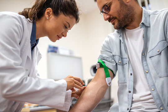 Female doctor prepares to draw blood from male patient. The patient's arm is secured with a tourniquet, and the doctor is focused on the procedure.