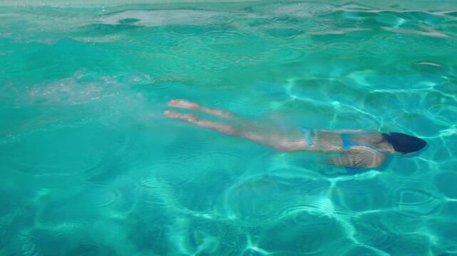 Slow motion of woman diving and swimming across pool, emerging smiling on ladder &ndash; joyful summer lifestyle in 4K