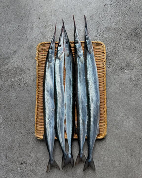 Pacific saury lined neatly on straw mat.
