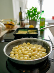 Golden Gnocchi Cooking in Pan with Fresh Herbs and Vegetables in Modern Bright Kitchen
