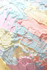 Fototapeta premium A close-up, high-angle shot captures a textured surface made of thick, pastel-colored paint. The colors soft pink, light yellow, mint green, and pale lavender are applied in broad.