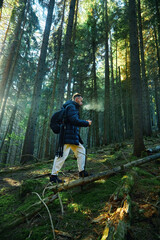 Obraz premium Man hiker with backpack walking through forest in Carpathian mountains enjoying river view.