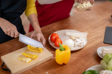 A woman is cutting vegetables on a wooden cutting board