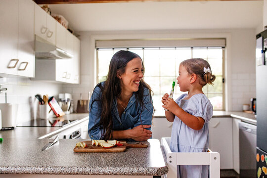 Toddler girl standing on a ladder looking at mum holding a food doypack.