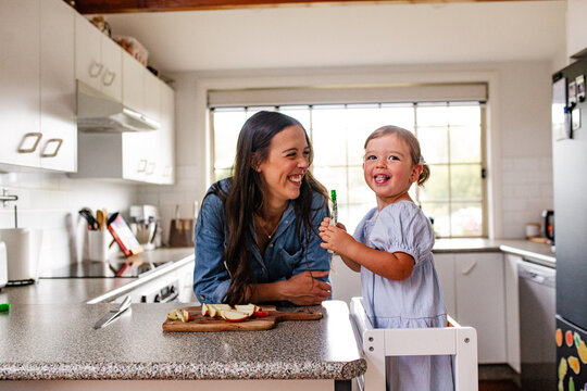 Happy toddler girl standing on a kitchen tower holding a food pouch
