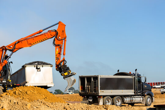 Excavator earthmoving equipment working on dirt pile at construction site beside truck