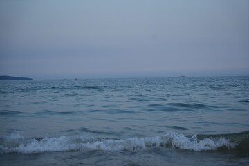 Calm sea at dawn with soft pastel blue and pink tones. Gentle waves approaching the shore under a peaceful, minimalistic horizon.