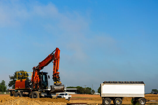 Excavator earthmoving equipment working on dirt pile at construction site beside truck