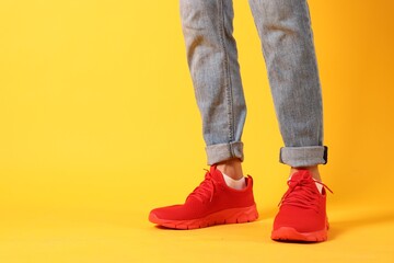 Man wearing pair of red sneakers on yellow background, closeup. Space for text