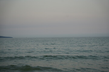 Calm sea at dawn with soft pastel blue and pink tones. Gentle waves approaching the shore under a peaceful, minimalistic horizon.