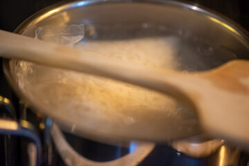 A candid kitchen scene showing a woman preparing rice, as boiling water steams from the pot