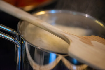 A candid kitchen scene showing a woman preparing rice, as boiling water steams from the pot
