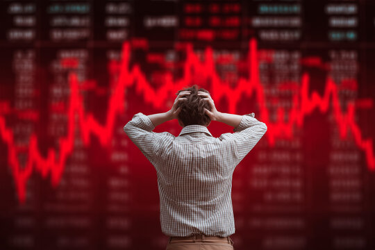 Stock market crash panic and investor stress. Man holding head in front of falling stock chart