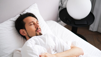 Portrait of a young brunette man sleeping soundly in a soft, cozy bed bathed in early morning light