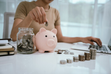An Asian woman is writing in a notebook and stacking coins and a piggy bank, which symbolizes...